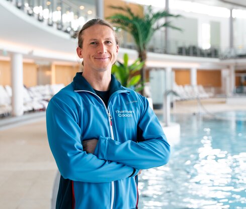 Thermencoach posiert vor dem Innenbecken der Therme des Spa Resort Geinberg | © Spa Resort Geinberg